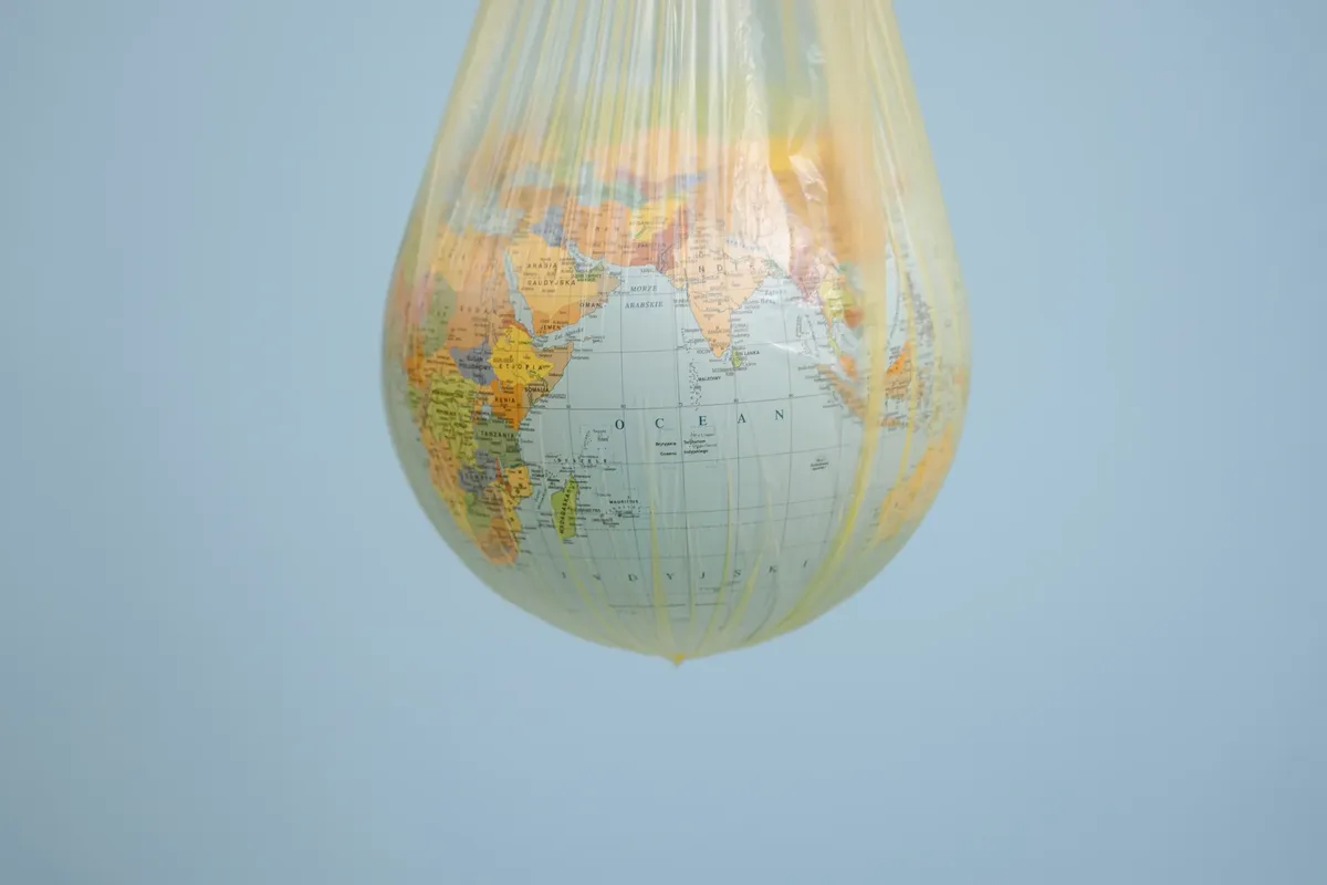 A globe wrapped in a plastic bag illustrating environmental concerns with a blue backdrop.