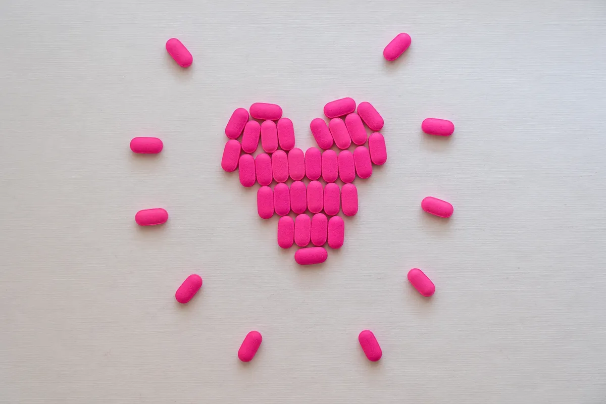 Pink pills arranged in a heart shape on a neutral surface. Perfect for health and medication themes.
